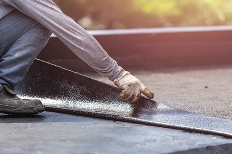 A man is applying a rubber mat to a flat roof, demonstrating careful installation techniques for durability.