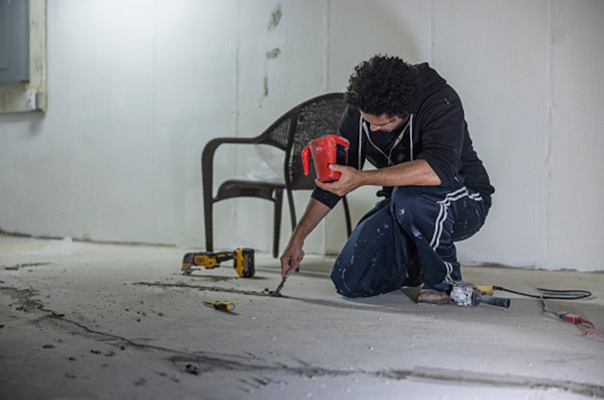  A man kneels on the floor, engaged in drilling, demonstrating a hands-on approach to home repairs.