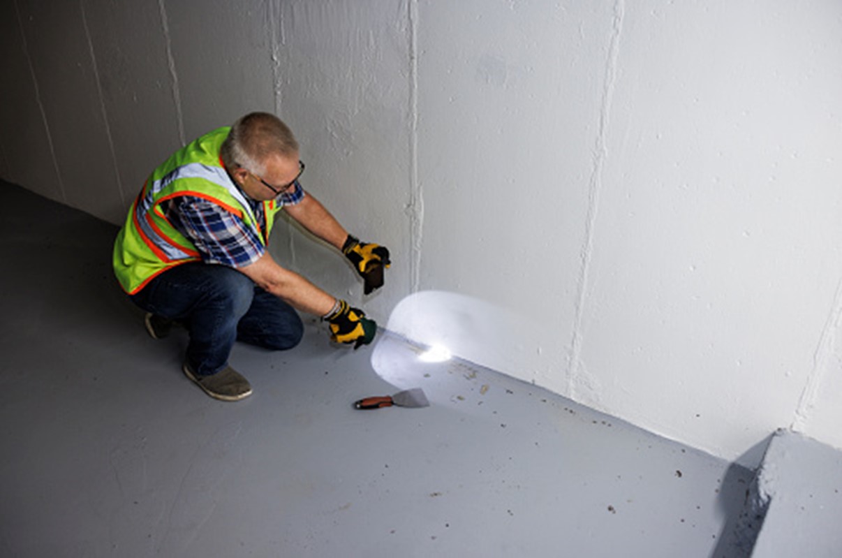 A man in a safety vest illuminates a wall with a flashlight, ensuring visibility in a dimly lit environment.